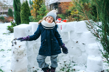 happy kid girl building snow castle on winter holidays. Seasonal outdoor activities.