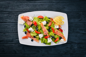 Salmon salad, feta cheese, salad leaves and fresh vegetables on the plate. On a wooden background. Top view. Free space for text.