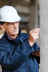 Senior construction manager controlling building site. He is holding tablet in his hands.