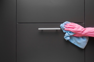 Employee hand in rubber protective glove with micro fiber cloth wiping a cupboards surfaces in the kitchen. Early spring or regular cleanup. Commercial cleaning company concept.