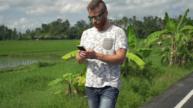 Young man with smartphone walking on road in country, super slow motion 120fps
