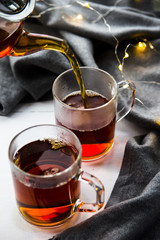 Pour black tea from a transparent teapot into a cup. Winter home concept