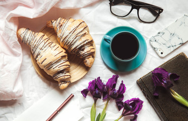Breakfast in the bed. Morning, croissant, coffee, flowers and a notebook with a pen. Planning