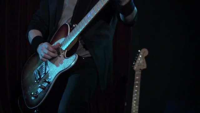 Man playing rock song on electric guitar in night club. close-up. Musician play wooden electric guitar on stage
