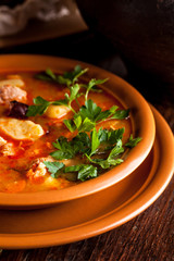 Traditional Russian and Ukrainian cuisine, lunch, first course, red soup in a clay dish on a wooden table