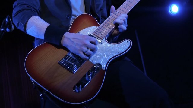 Man playing rock song on electric guitar in night club. close-up. Musician play wooden electric guitar on stage