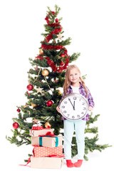 Portrait of little girl with clock showing five minutes to twelve standing near Christmas tree on white background