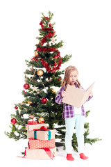 Portrait of cute little girl reading book near Christmas tree on white background