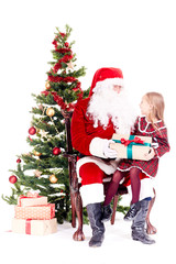 Cute little girl receiving gift from Santa Claus sitting on his lap near Christmas tree