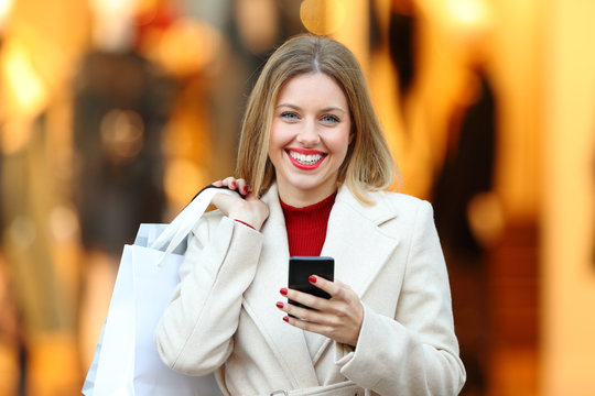 Shopper holding shopping bags and phone looking at you