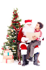Fototapeta na wymiar Santa Claus reading book for mixed-race little boy who is sitting on his lap near Christmas tree