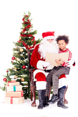 Fototapeta na wymiar Santa Claus reading book for mixed-race little boy who is sitting on his lap near Christmas tree