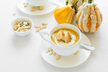 Two cups with fresh pumpkin cream soup decorated cream, seeds and crackers on white table cloth