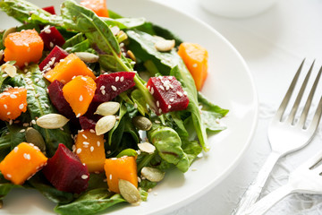 Fresh autumn salad with marinated pumpkin and beetroot, spinach leaves,olive oil, sesame and pumpkin seeds on white table cloth. Space for copy