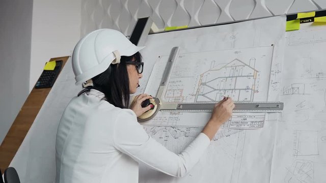 A close-up of a female architect which has a helmet and glasses is working on a project of a residential building