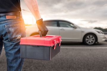 The abstract image of the back of technician hold a toolbox and blurred car is backdrop. the concept of automotive, repairing, mechanical, vehicle and technology.