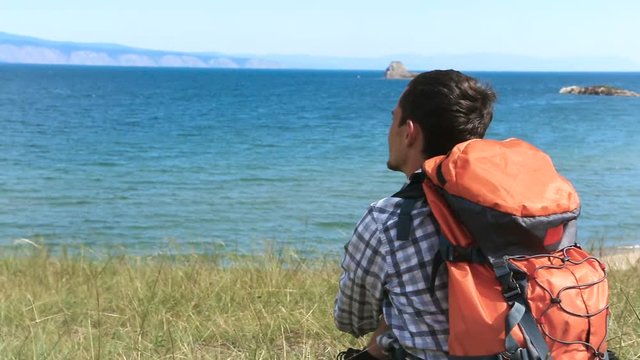 Hiker relaxing on a shore of lake Baikal. Traveler young brunette man looking at blue water of lake baikal. Olkhon Island, Baikal, Russia, Siberia