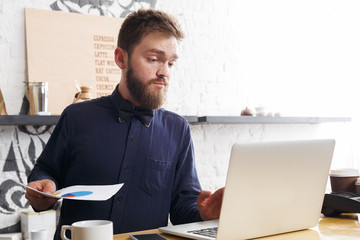 Fototapeta premium Pensive barman working on laptop at bar counter