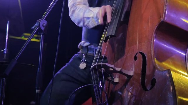 Musician playing contrabass close-up. Man artist play wooden double bass on stage dark background
