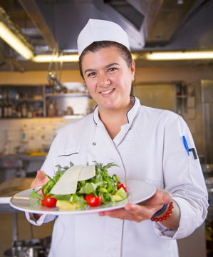 Proud female chef holding a plate with salat in a restaurant kitchen