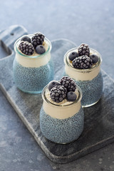 Fototapeta na wymiar Three Mini Vegan Blue Spirulina Chia Puddings Topped with Whipped Coconut Cream and Frozen Berries