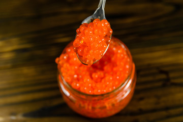 Red caviar in a spoon above the glass jar