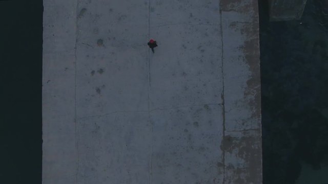 Aerial drone top view footage of small figure of lonely man, walk in middle of concrete pier on cold winter morning. Dreams and thinks about future, looks around at sea waves, epic and romantic