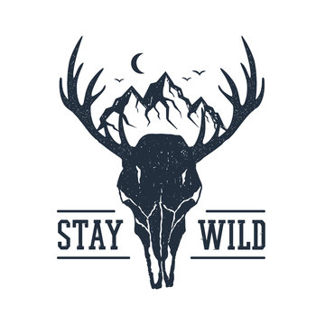 Hand drawn inspirational label with mountains and deer skull textured vector illustrations and "Stay wild" lettering.