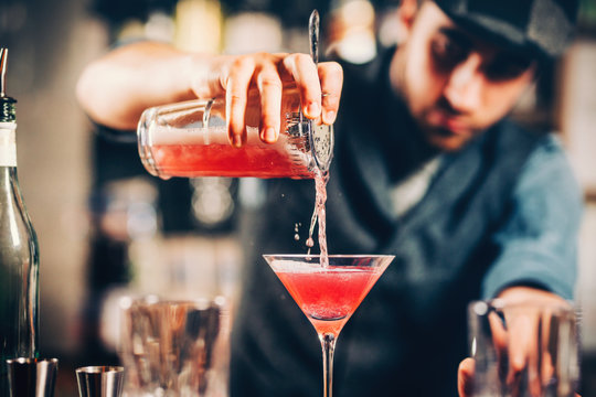 barman preparing and pouring red cocktail in martini class. cosmopolitan cocktail with bar background