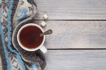 A cup of tea and a knitted scarf on the background of a white wo