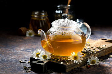 glass teapot of fragrant chamomile tea on dark background