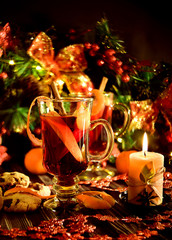 Christmas and New Year mulled wine with cinnamon, cardamom and anise on a background of spruce branches, snowflakes and burning candles, dark toned image, selective focus