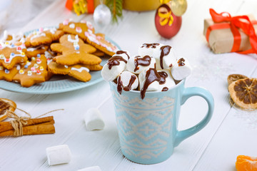Traditional hot chocolate with marshmallows and chocolate on the white wooden table with christmas tree, decor , gift boxes, cookies and spices. Christmas drink theme. Selective focus.