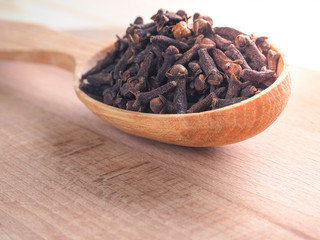 Spice cloves and a wooden spoon on a wooden table.
