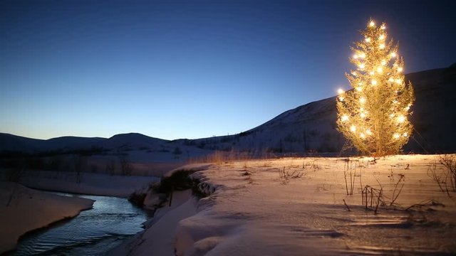 christmas tree glowing lights by mountain stream in winter, snow and blue sky at dawn, Iceland 3