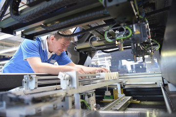 Arbeiter in der elektronikfertigung bestückt eine Maschine zur Herstellung von Platinen // Workers...