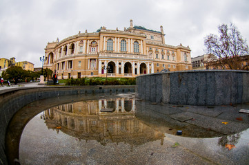 Square next to Odessa Opera House in autumn with grey empty stone fountain without water. Reflection of the building in the puddle