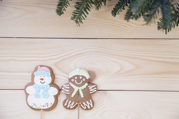 Christmas light wooden background with fir tree branches and a gingerbread man and glazed snowman. Close up. Copyspace