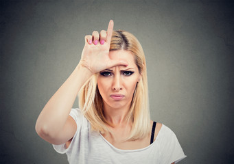 Closeup portrait unhappy woman giving loser sign on forehead, looking at you with anger and hatred...