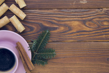 Christmas rustic wooden background with fir tree branches. A hot espresso in a pink porcelian cup with sticks of cinnamon on a saucer and cookies. Top view. Close up. Copyspace