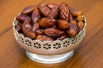Dates fruit on a silver bowl on wooden table. The Muslim feast of the holy month of Ramadan Kareem