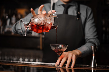 Barman in a tie and apron pouring red alcoholic drink in a cocktail glass