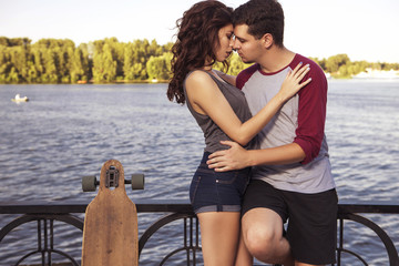 Young beautiful brunette caucasian sexy adult woman and men couple in love on a date outdoors in city, having fun skateboarding (on longboards). Summer weather