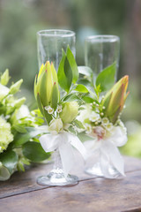 Bouquet of eustoma roses and glassess decorated with flowers lay on wooden table on a wedding ceremony. Soft day light, outdoor in garden