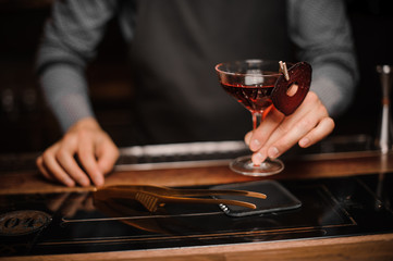 Barman hand holding a glass of red decorated alcoholic drink