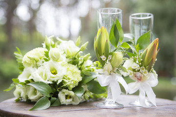 Bouquet of eustoma roses and glassess decorated with flowers lay on wooden table on a wedding ceremony. Soft day light, outdoor in garden