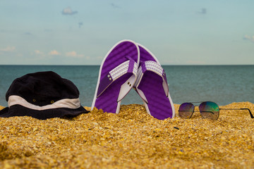 Pair of flip flops, hat and sunglasses on a sandy sea beach