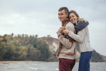 Happy thoughtful couple standing on a rock beach near sea hugging each other in cold foggy cloudy autumn weather. Copy space