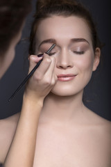 Make-up artist applying make up beautiful brunette caucasian woman with fresh clean skin and neutral nude makeup and ponytail hairstyle. neutral background. Young girl. Skincare. Copy space
