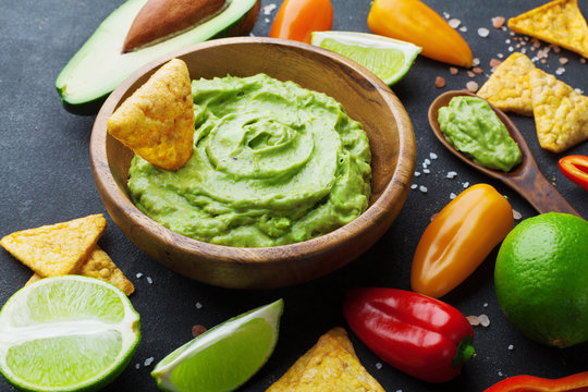Guacamole sauce with ingredients avocado, lime and nachos on black table. Traditional mexican food.